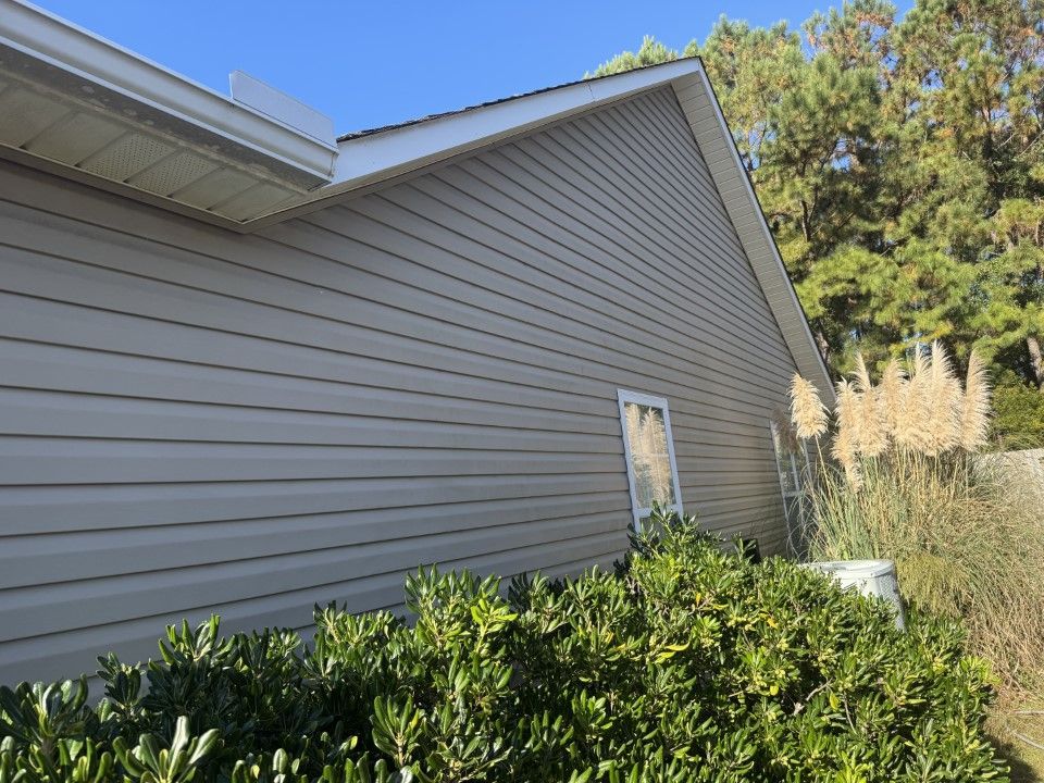 Tan siding on a house with white trim. A window and bushes are in view.