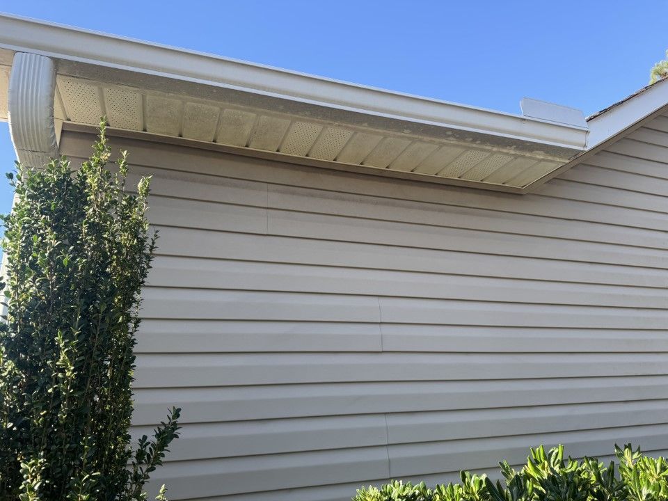 Beige siding and soffit on a house with a bush in front, under a clear blue sky.