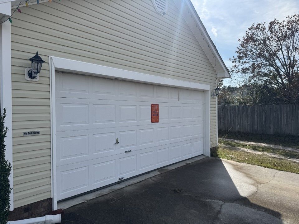White garage door on a beige house with a driveway. Bright sunlight.