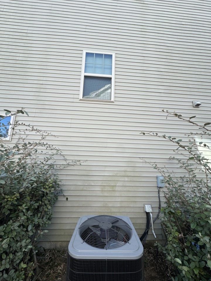 Air conditioning unit below a window on a gray-sided building with climbing vines.