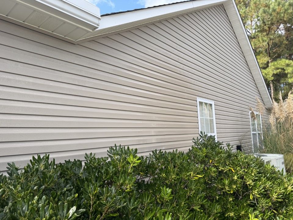 Tan vinyl siding on a house with white trim. Green bushes in the foreground.