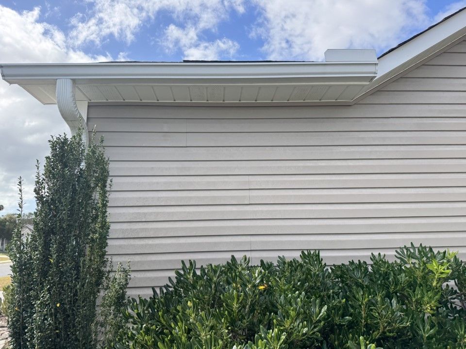 Beige siding on a house with white gutters and trim, blue sky with clouds in the background.