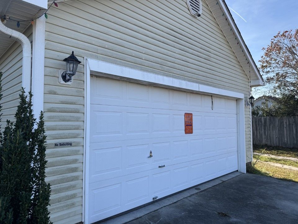 White garage door on beige house with a light fixture and siding, on a sunny day.