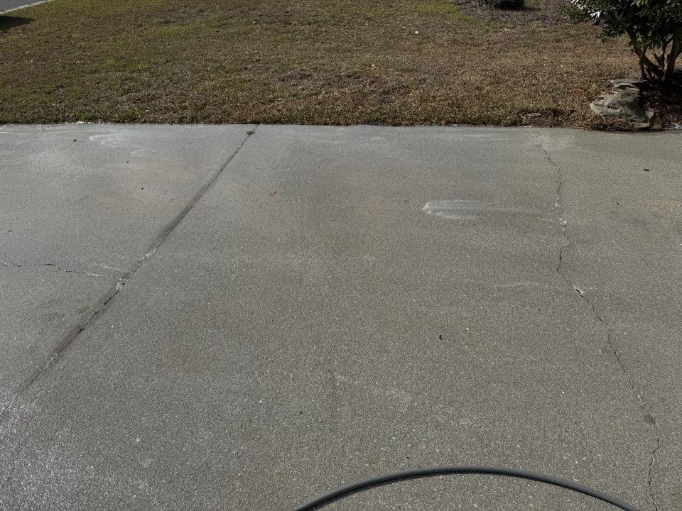 Gray concrete driveway with long crack, in front of a brown and green grass area.