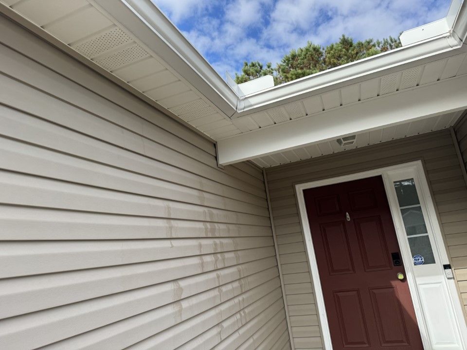 Beige siding and a burgundy door on a house, with a cloudy sky overhead.