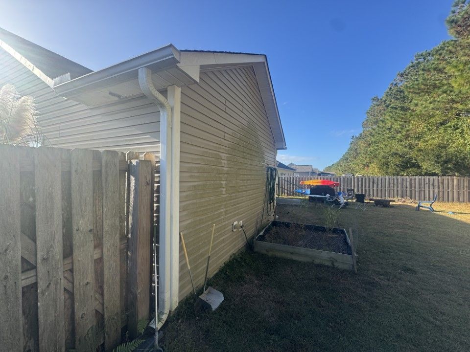Beige house siding with a wooden fence and backyard on a sunny day.