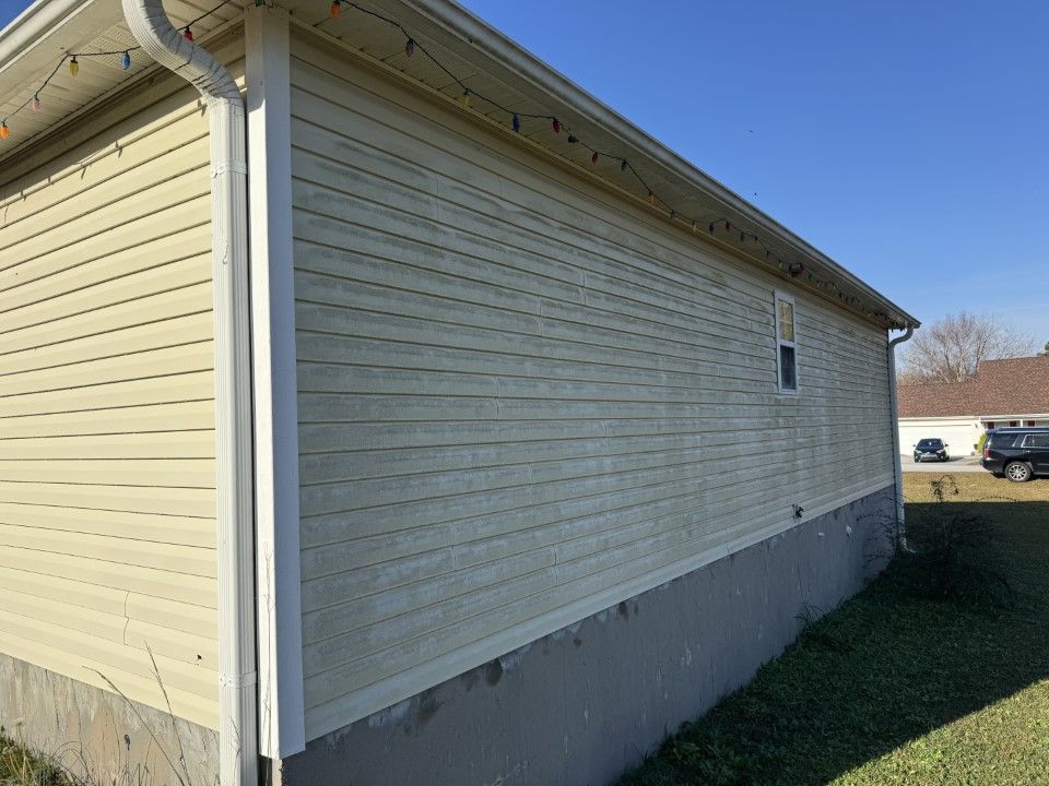 Side of a light yellow vinyl-sided building with white trim, a small window, and a concrete foundation under a clear blue sky.