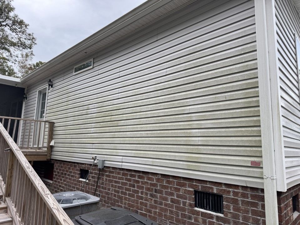 Side of a house with dirty, light-colored vinyl siding and a brick foundation, plus a wooden deck.