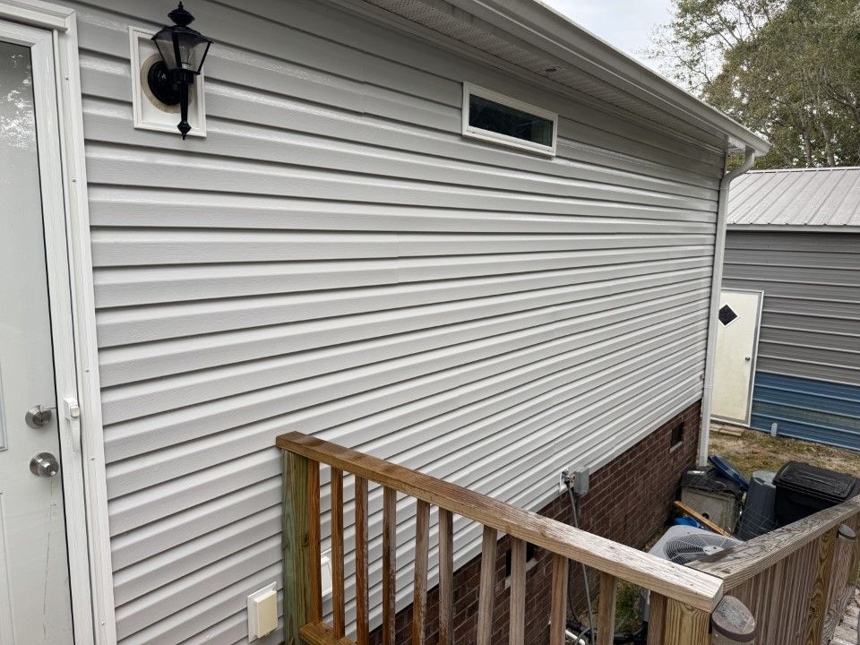 Gray vinyl siding on a building with a wooden deck in front. A small window and a light are visible.
