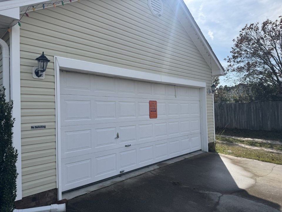 White garage door on a tan house exterior with a small, orange notice posted on it.