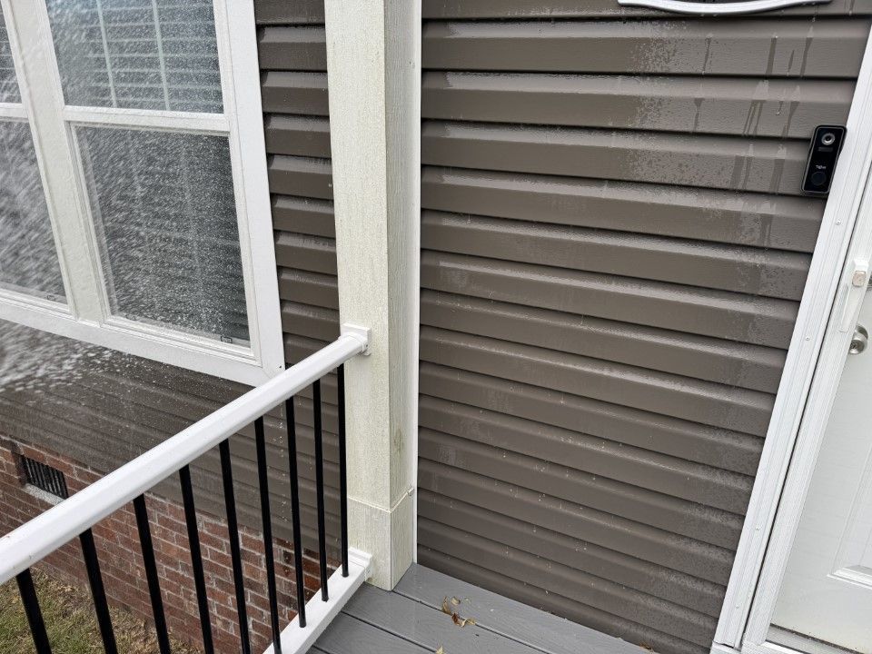 Exterior of a building with brown siding, a white window, and a small porch with a railing.