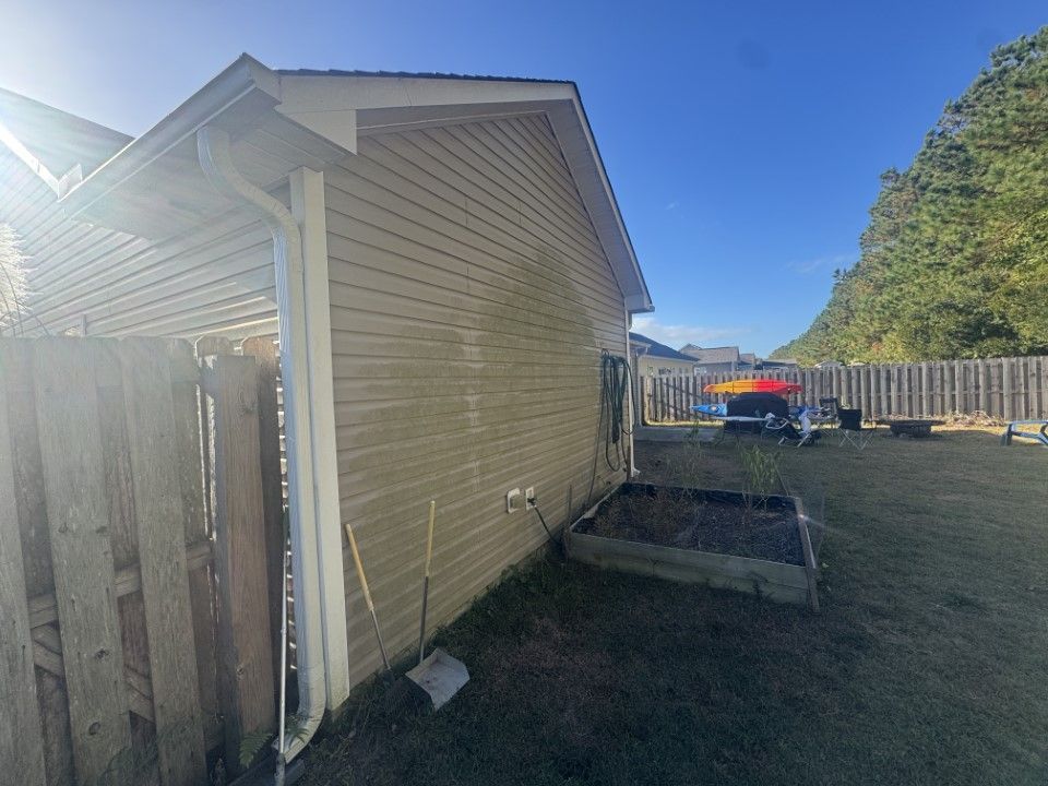 Side of a beige house with a wooden fence. A raised garden bed and backyard are visible under a blue sky.