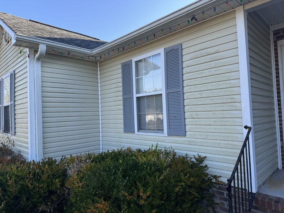 Light-colored house with a window, gray shutters, and shrubs in front.