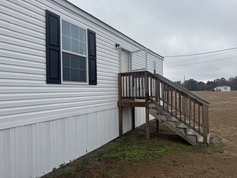 Mobile home with white siding, black shutters, and wooden stairs leading to the door.
