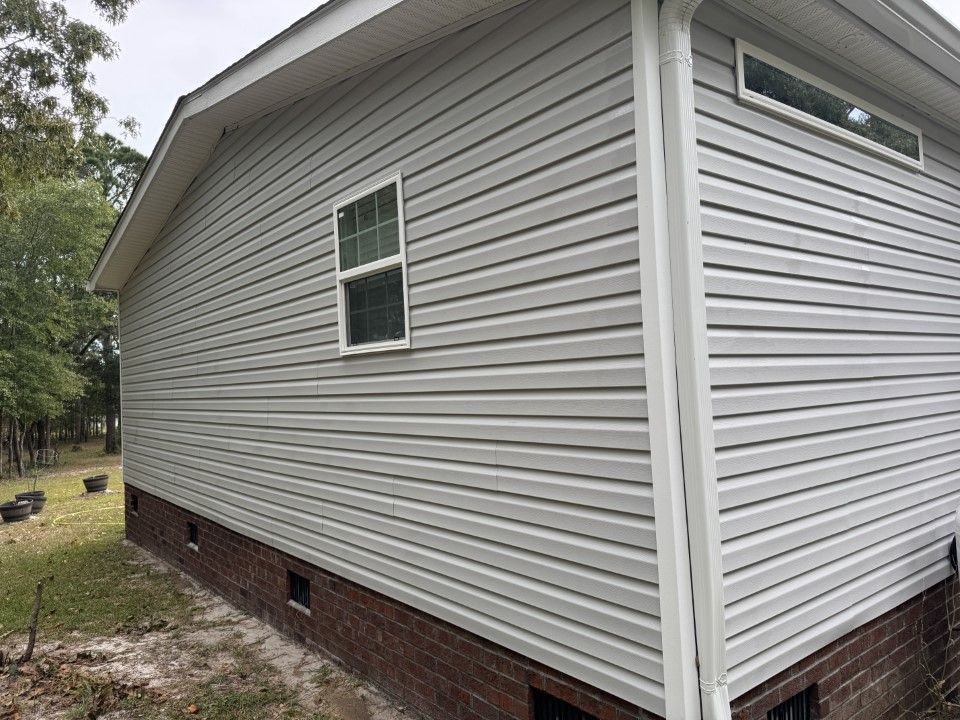 Gray vinyl siding on a house with a brick foundation and white trim.