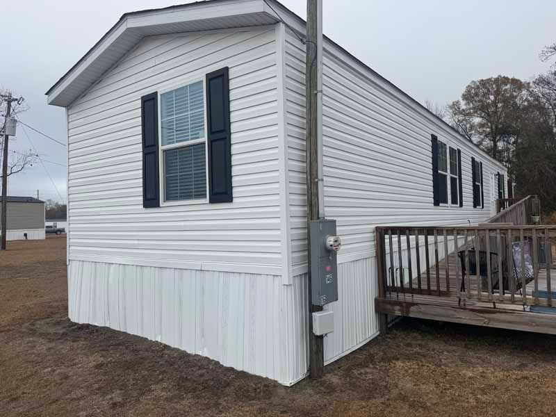 White mobile home with dark shutters and attached wooden deck.
