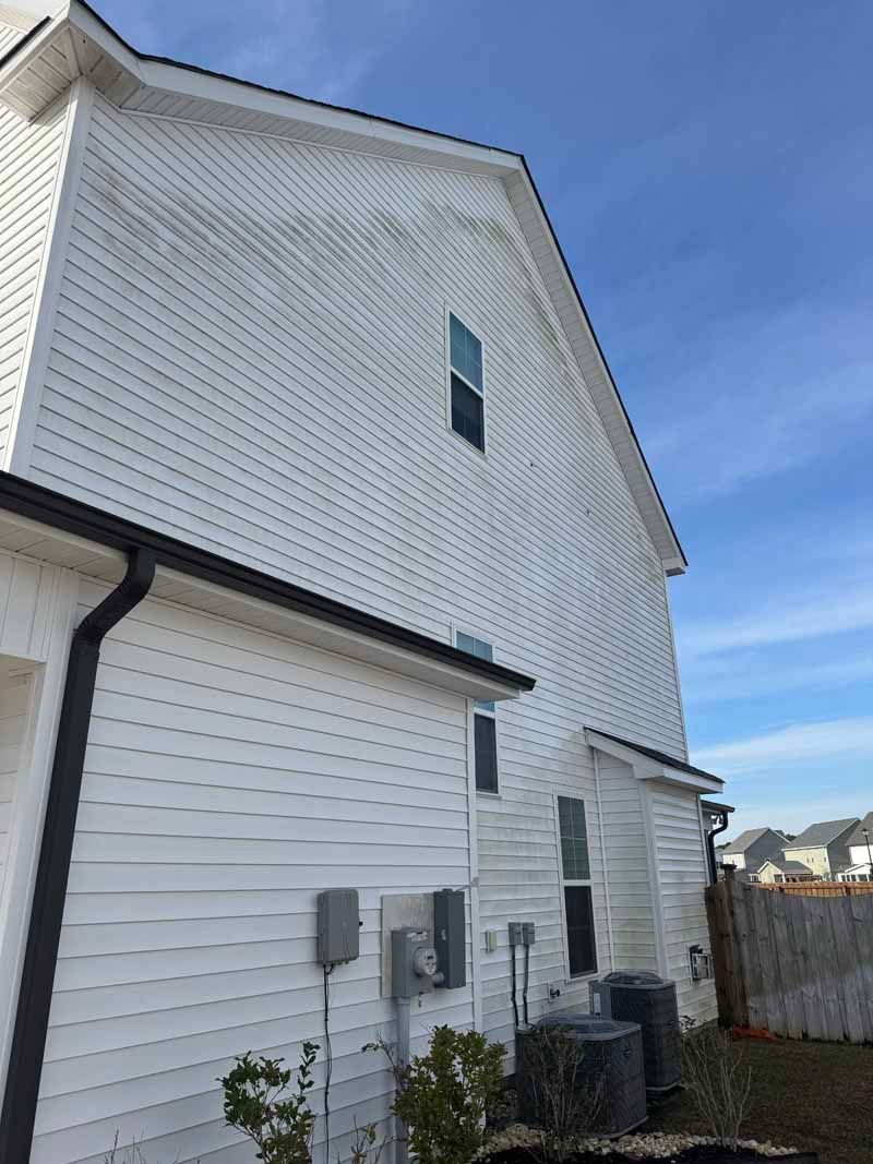 White vinyl siding on a house with dark roof and trim. Exterior shows dirt streaks against a blue sky.