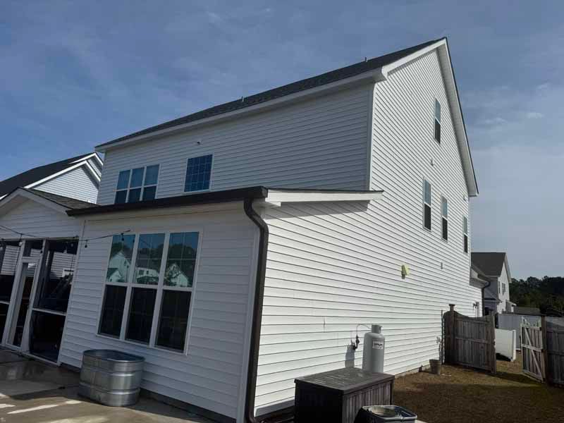 White two-story house with black trim, windows, and gutters. A small structure is attached with a screened area.