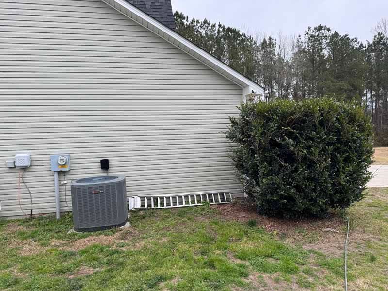 Side of a light gray house with an air conditioner unit and a green bush next to it.