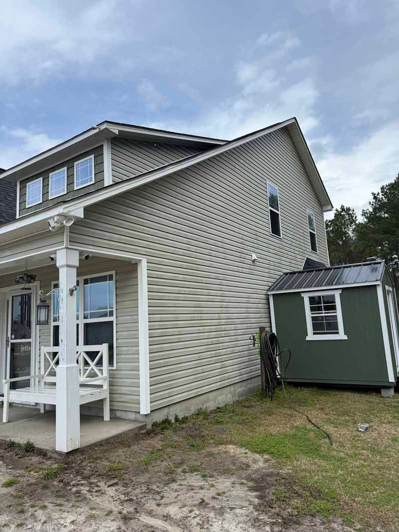 Two-story house with unique siding pattern, small green shed, porch with white columns, and cloudy sky.