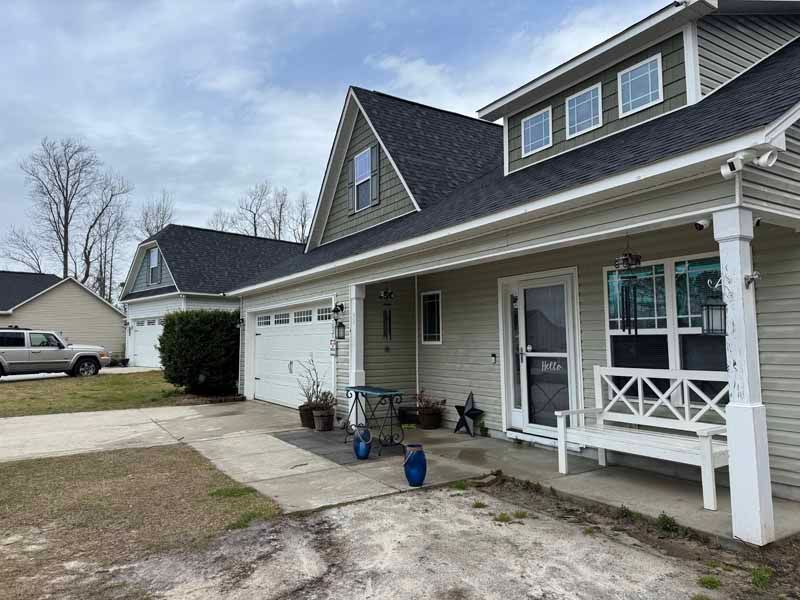 Suburban house with gray siding, garage, porch, and dark roof on a cloudy day.