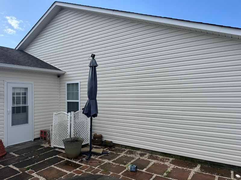 Exterior of a building with white siding, door, and a patio with a closed umbrella.