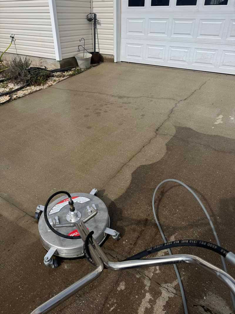 A concrete driveway being pressure washed with a circular surface cleaner.