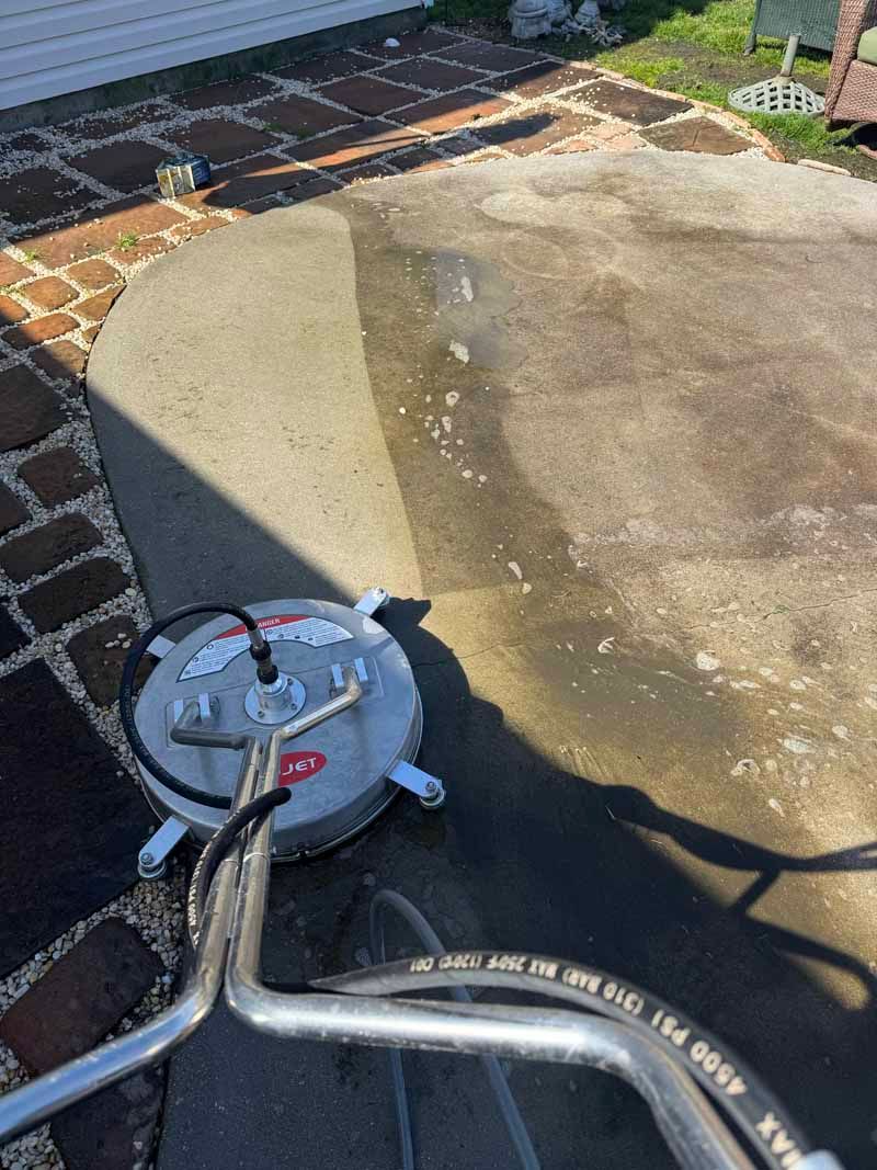 Power washer cleaning a concrete patio, revealing a lighter, cleaner surface.