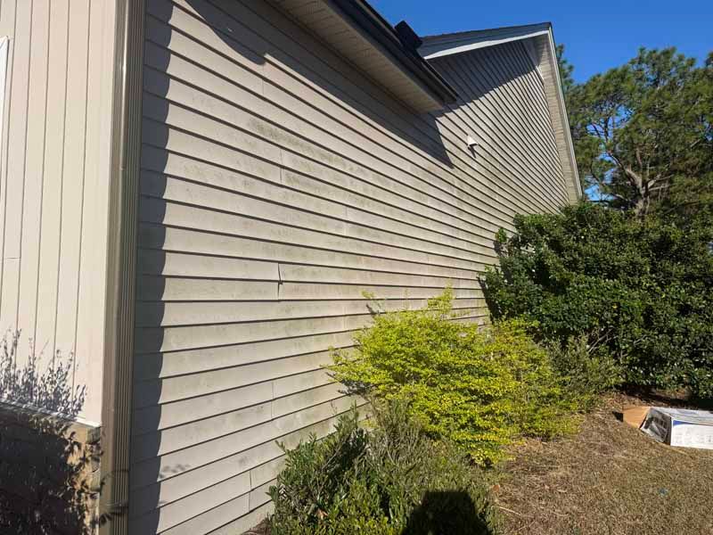 Beige siding on a house, with green bushes in front.