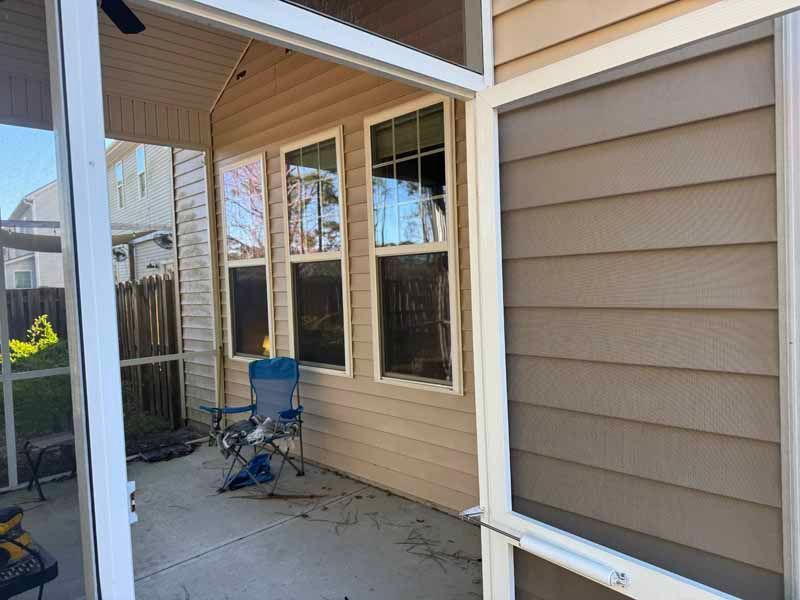 Screened porch with windows, a chair, and tan siding. Sunlight and shadows are visible.