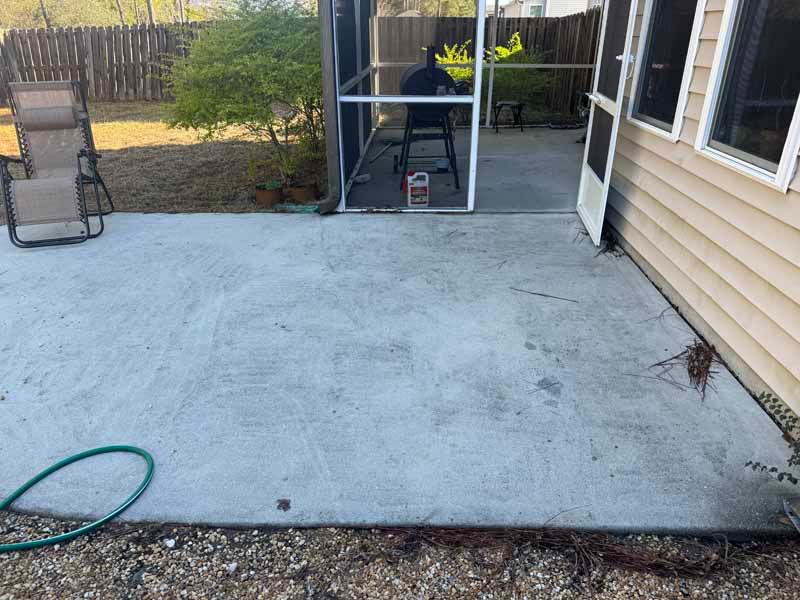 Gray concrete patio with a screen enclosure and a house on the right. Lawn chair on the left.