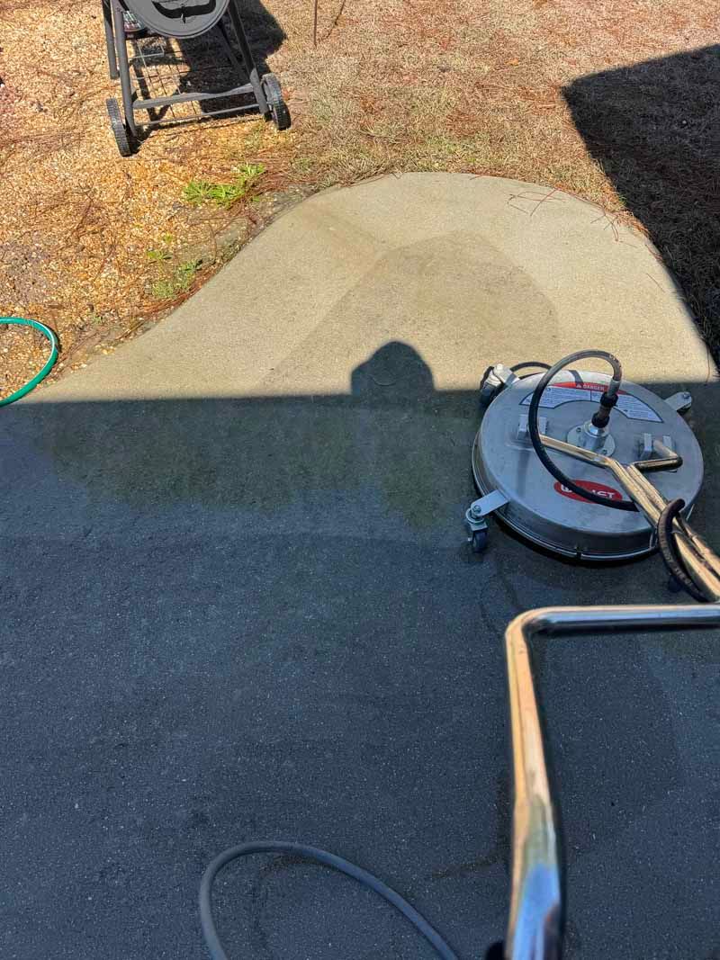 A person using a surface cleaner on a concrete patio. The cleaned area is lighter in color.