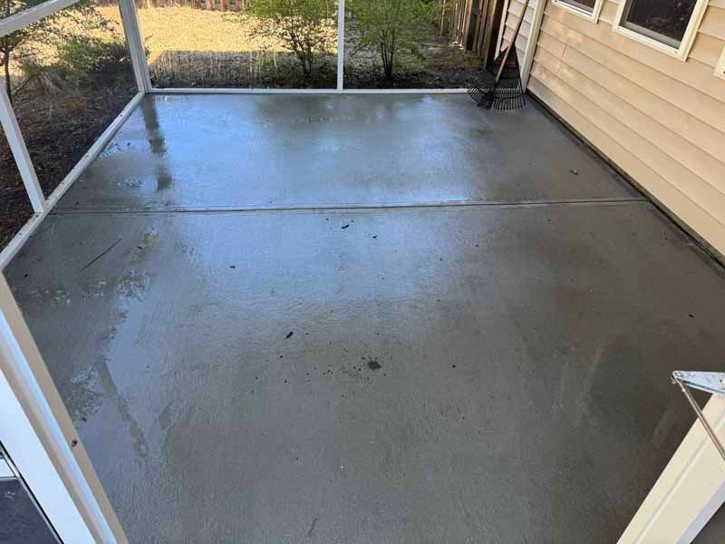A freshly poured, wet concrete patio surrounded by a screen enclosure and a light-colored house.