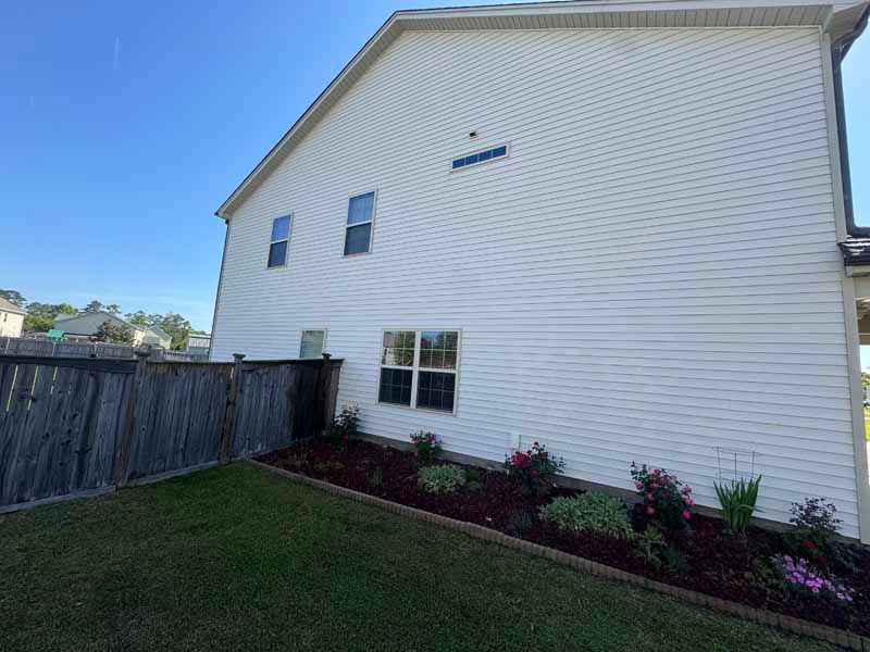 Side view of a two-story white house with a landscaped garden bed and a wooden fence.