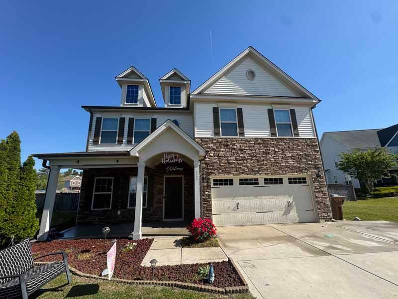 Two-story house with stone facade, beige siding, white trim, and a blue sky.