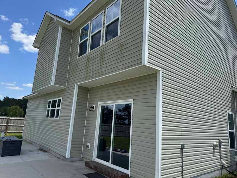Two-story house with light green siding and white trim against a blue sky.