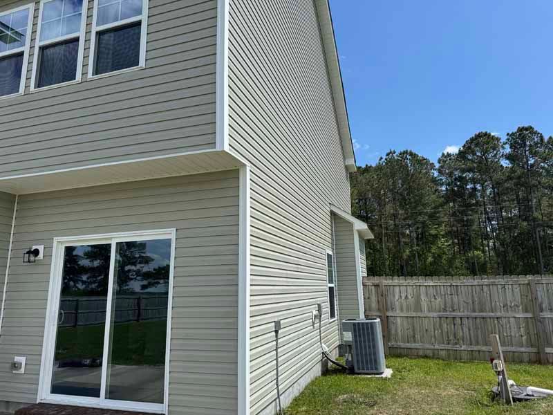 Side view of a two-story house with gray siding, sliding glass door, and air conditioning unit on green grass.