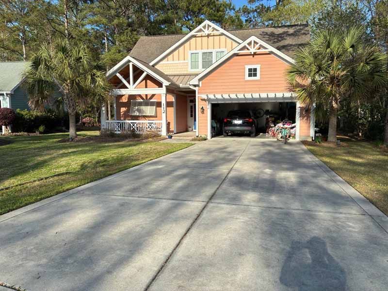 House with salmon-colored exterior, attached garage, and long driveway. Palm trees and green lawn surround it.