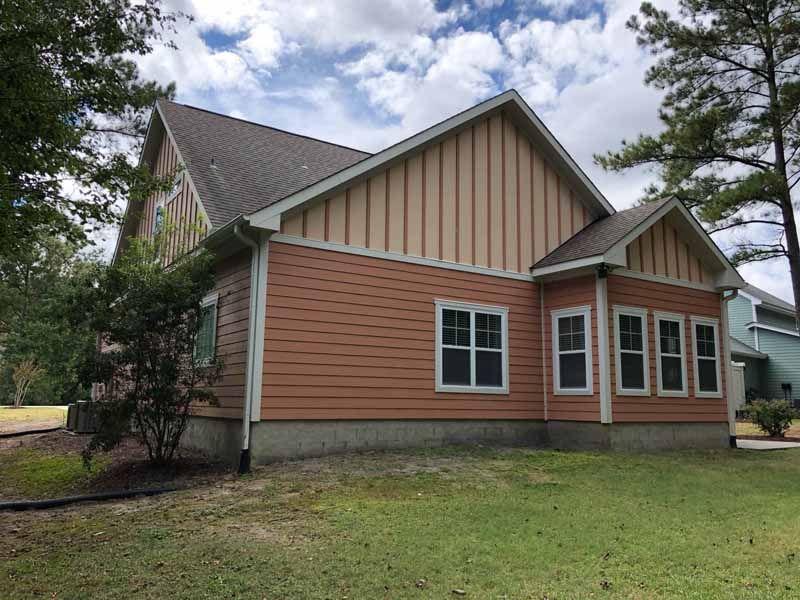 Side view of a house with orange siding, white windows, and a brown roof against a cloudy sky.