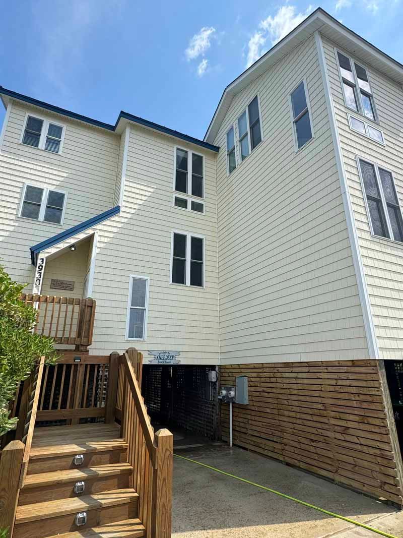 Two-story beige house with wooden stairs and blue trim against a blue sky.