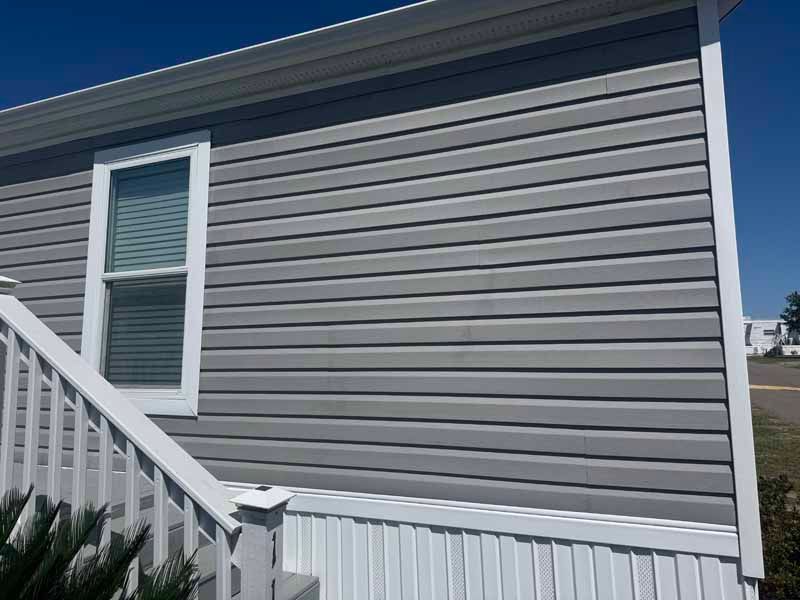 Gray vinyl siding on a house with a white window and trim, blue sky.