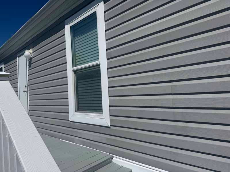 Side view of a house with gray siding, white window and door trim, and a small deck with railing.