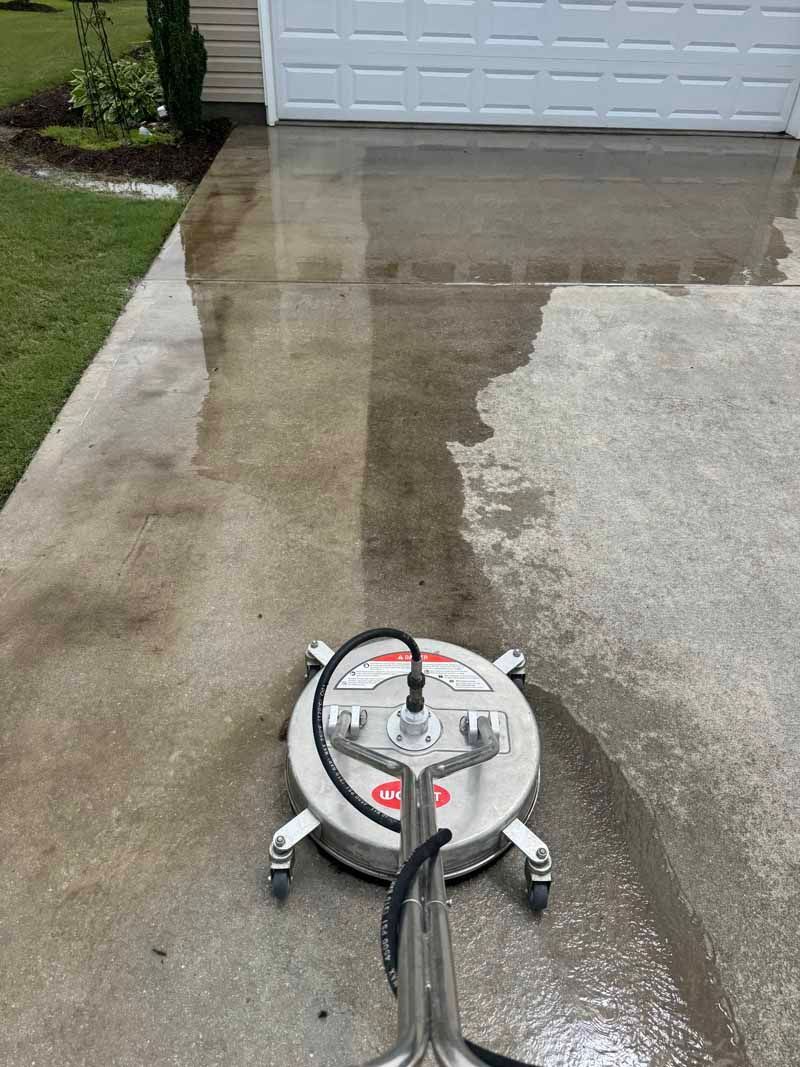 A concrete driveway being power washed with a circular surface cleaner.