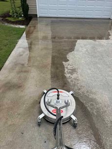 A concrete driveway being power washed with a circular surface cleaner.