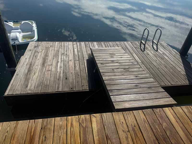 Wooden dock with ramp and ladder over water; a small boat is docked nearby.