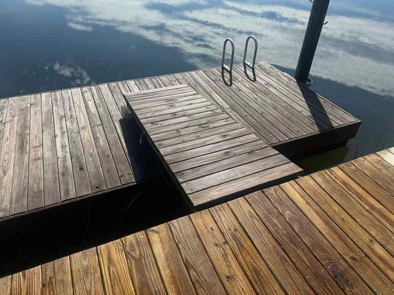 Wooden dock with a ramp leading to a floating platform and a ladder, on calm water.