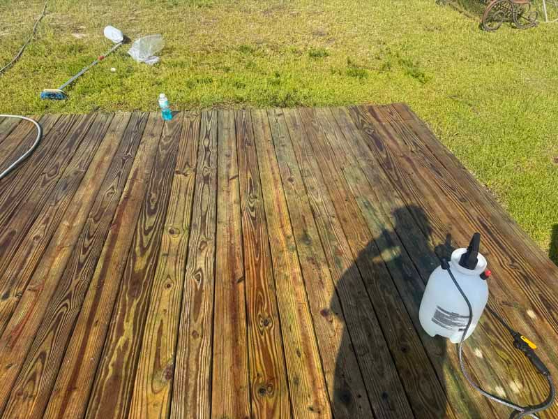 Wooden deck being cleaned with a sprayer; a grassy yard is in the background.
