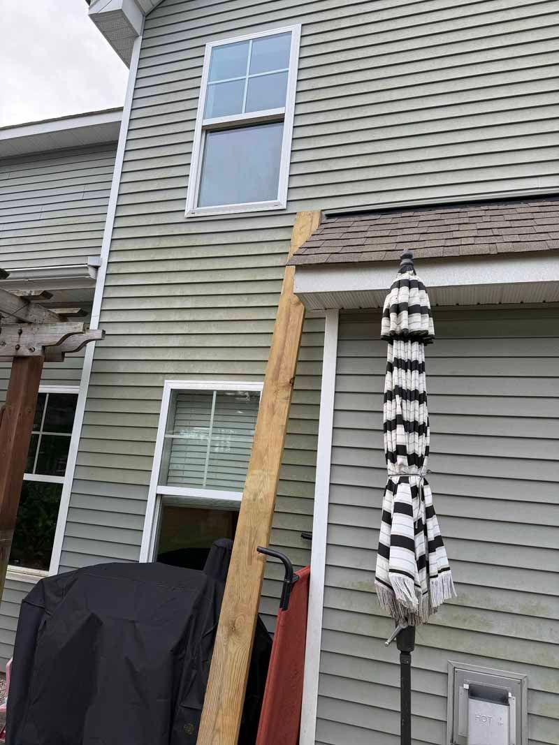 Gray house exterior with two windows, a wood plank, and a black and white umbrella.