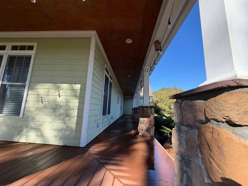 Covered porch with wood flooring, stone columns, green siding, and a blue sky.