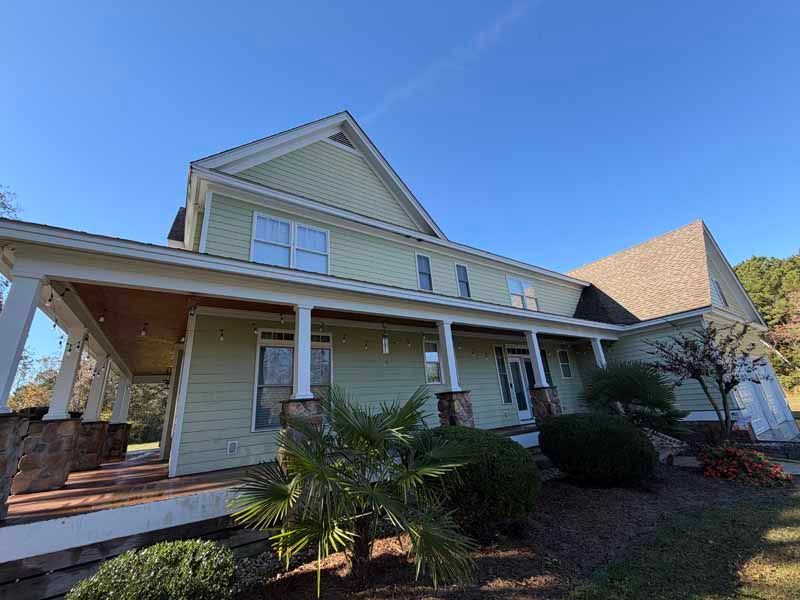 Green house with a covered porch and brown roof under a blue sky.